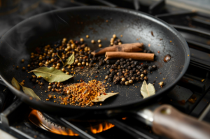 A pan of roasting spices cinnamon, pepper, bay leaf, coriander seeds for Mutton Dhansak recipe