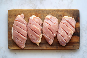 Four raw chicken breasts arranged neatly on a wooden cutting board, each with a pocket made by slicing horizontally for marination purpose in the preparation of Stuffed tandoori chicken breasts